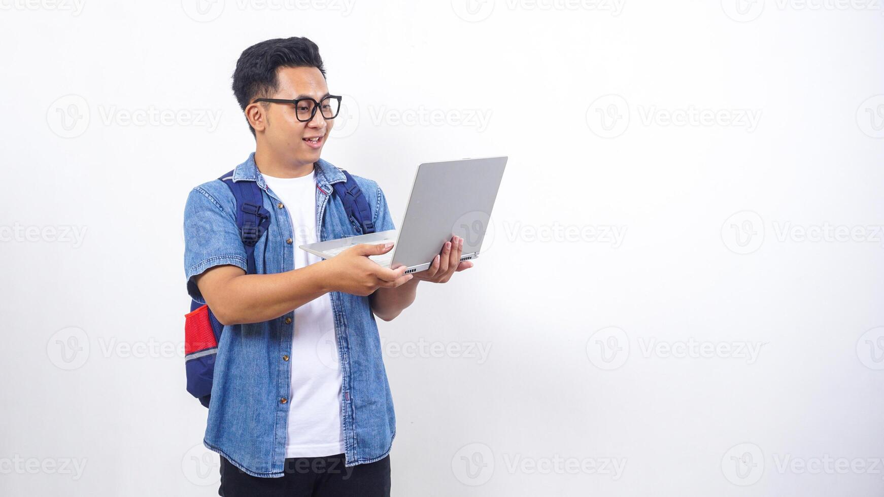 Happy young Asian male university student in casual outfit with backpack and open laptop isolated on white background with copy space photo