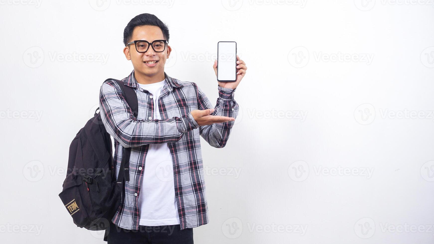 Portrait of cheerful young Asian male college student with a backpack showing blank screen of smartphone mock up isolated on white background photo