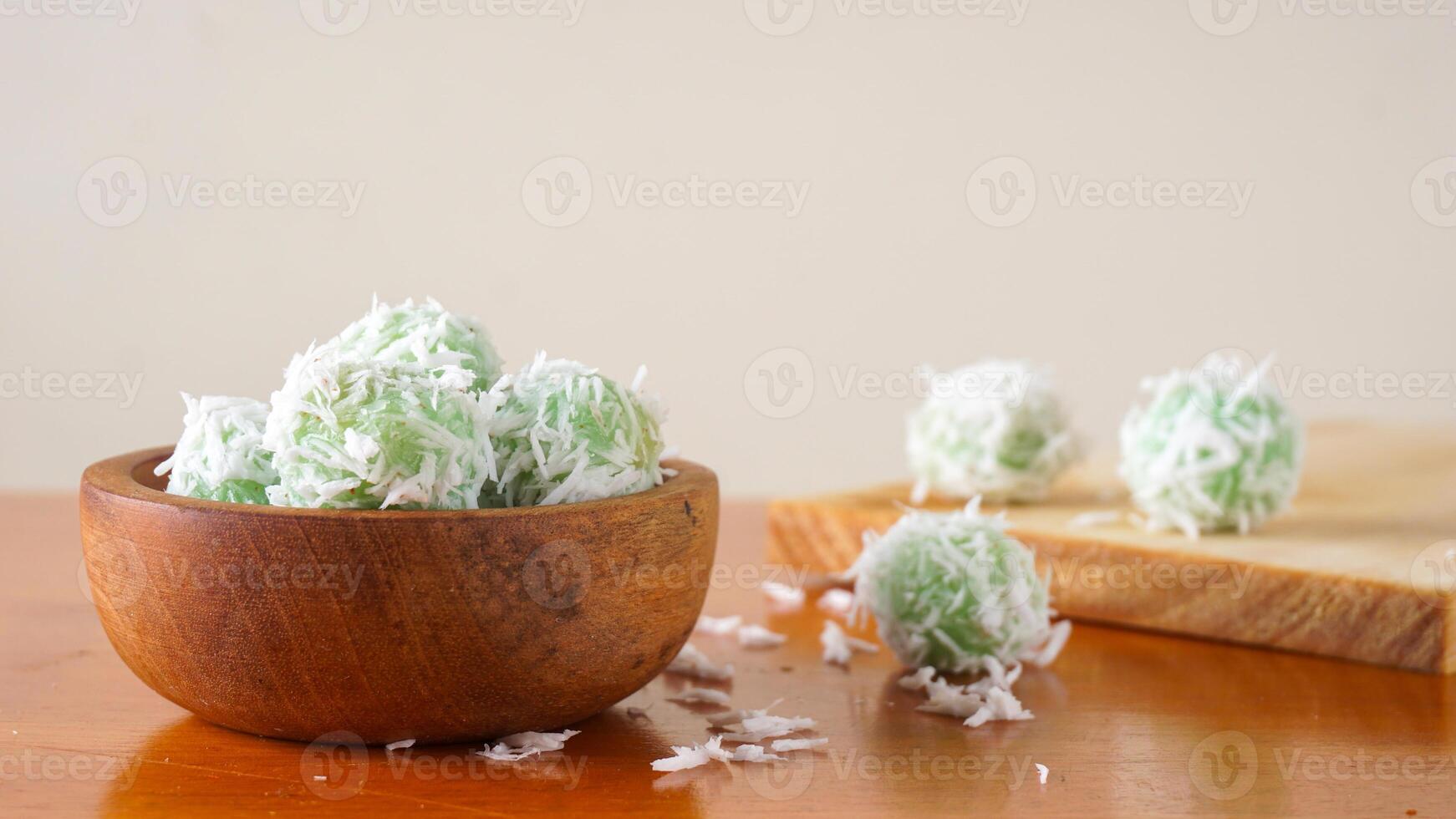 Klepon is a popular traditional Indonesian snack made from green sticky rice balls and rolled in grated coconut on wooden bowl isolated on white background photo