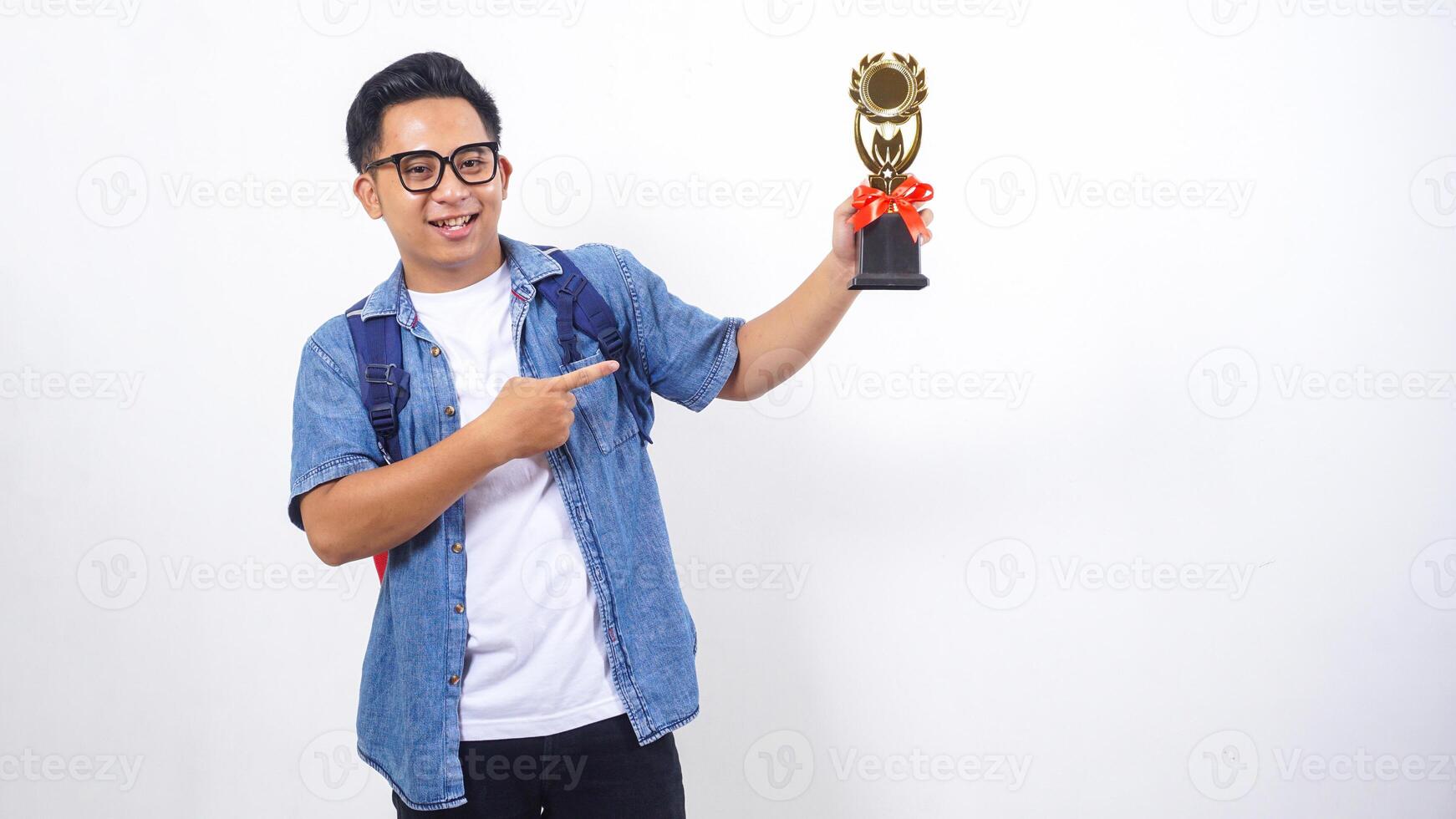 Portrait of handsome young Asian male university student in casual outfit with backpack is holding trophy isolated on white background photo