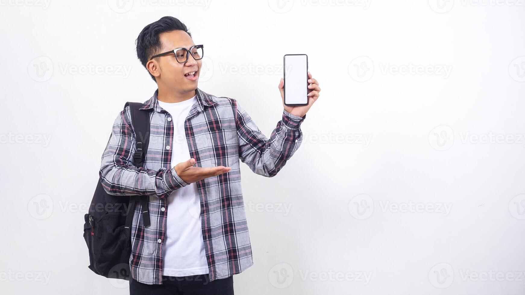 Portrait of young Asian male college student with a backpack showing blank screen of smartphone mock up isolated on white background photo