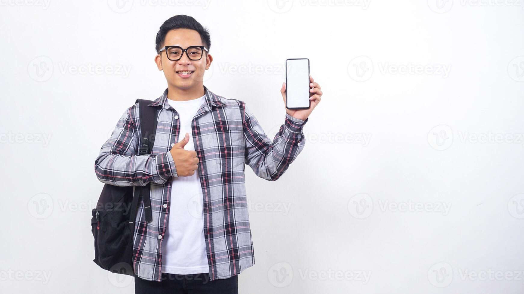 Portrait of smiling young Asian male college student with a backpack showing blank screen of smartphone mock up isolated on white background photo