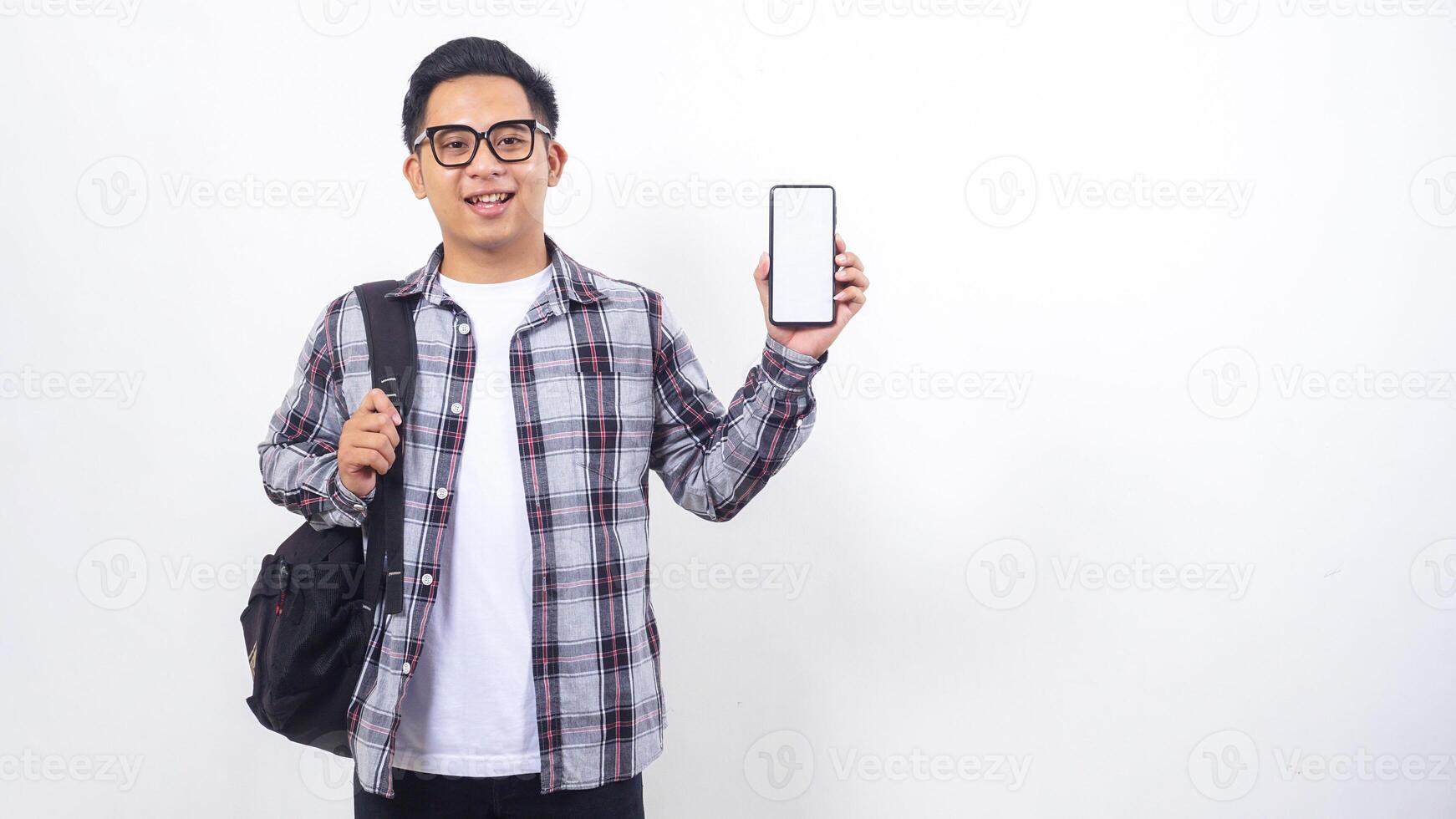 Young Asian male college student with a backpack showing blank screen of smartphone mock up isolated on white background photo