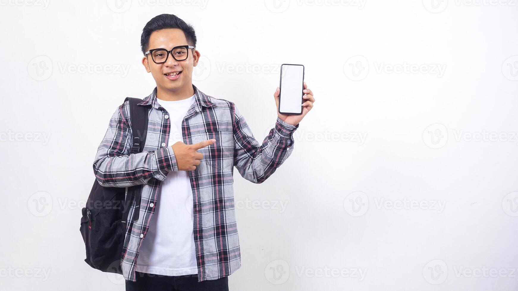 Portrait of handsome young Asian male college student with a backpack showing blank screen of smartphone mock up isolated on white background photo