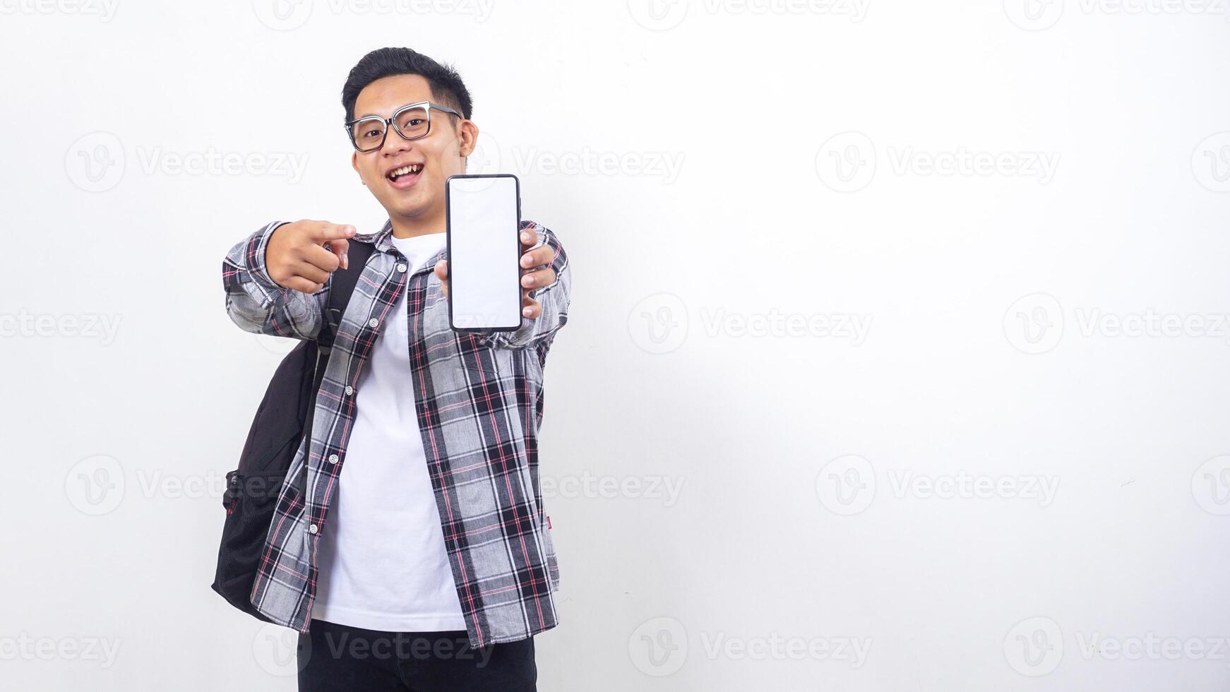 Excited young Asian male college student with a backpack showing blank screen of smartphone mock up isolated on white background photo