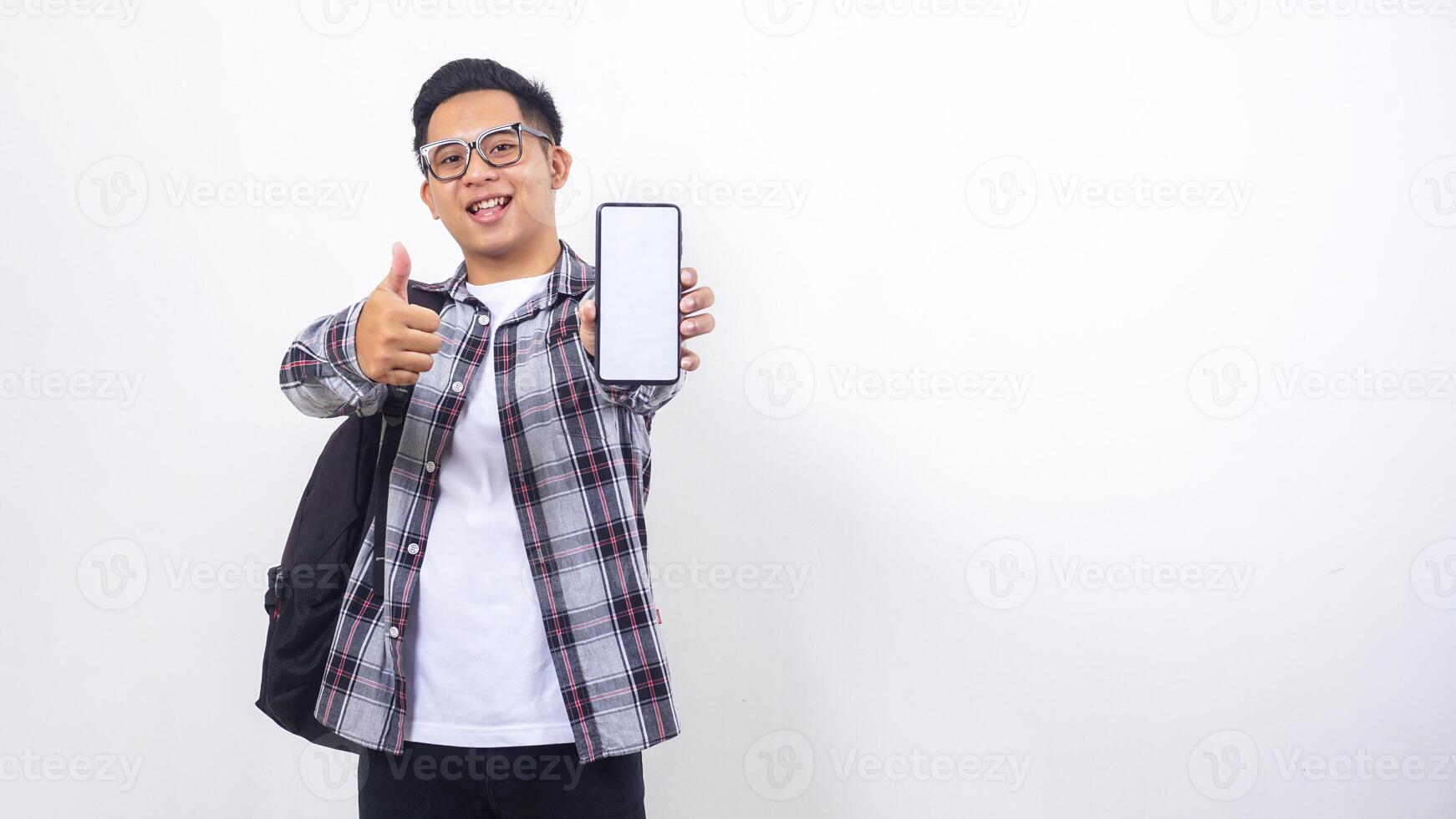 Cheerful young Asian male college student with a backpack showing blank screen of smartphone mock up isolated on white background photo