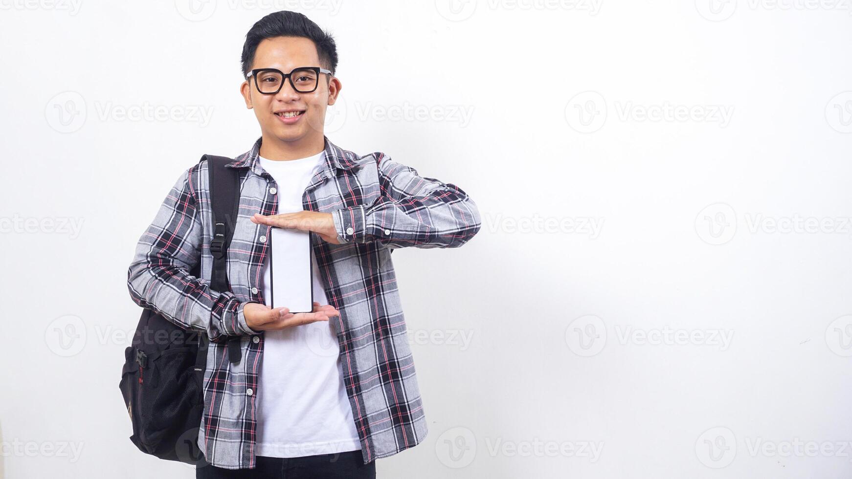 Portrait of smart young Asian male college student with a backpack showing blank screen of smartphone mock up isolated on white background photo