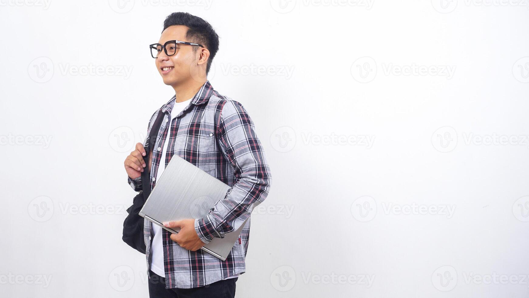 Side view of smiling young Asian male college student with a backpack and holding laptop notebook isolated on white background photo