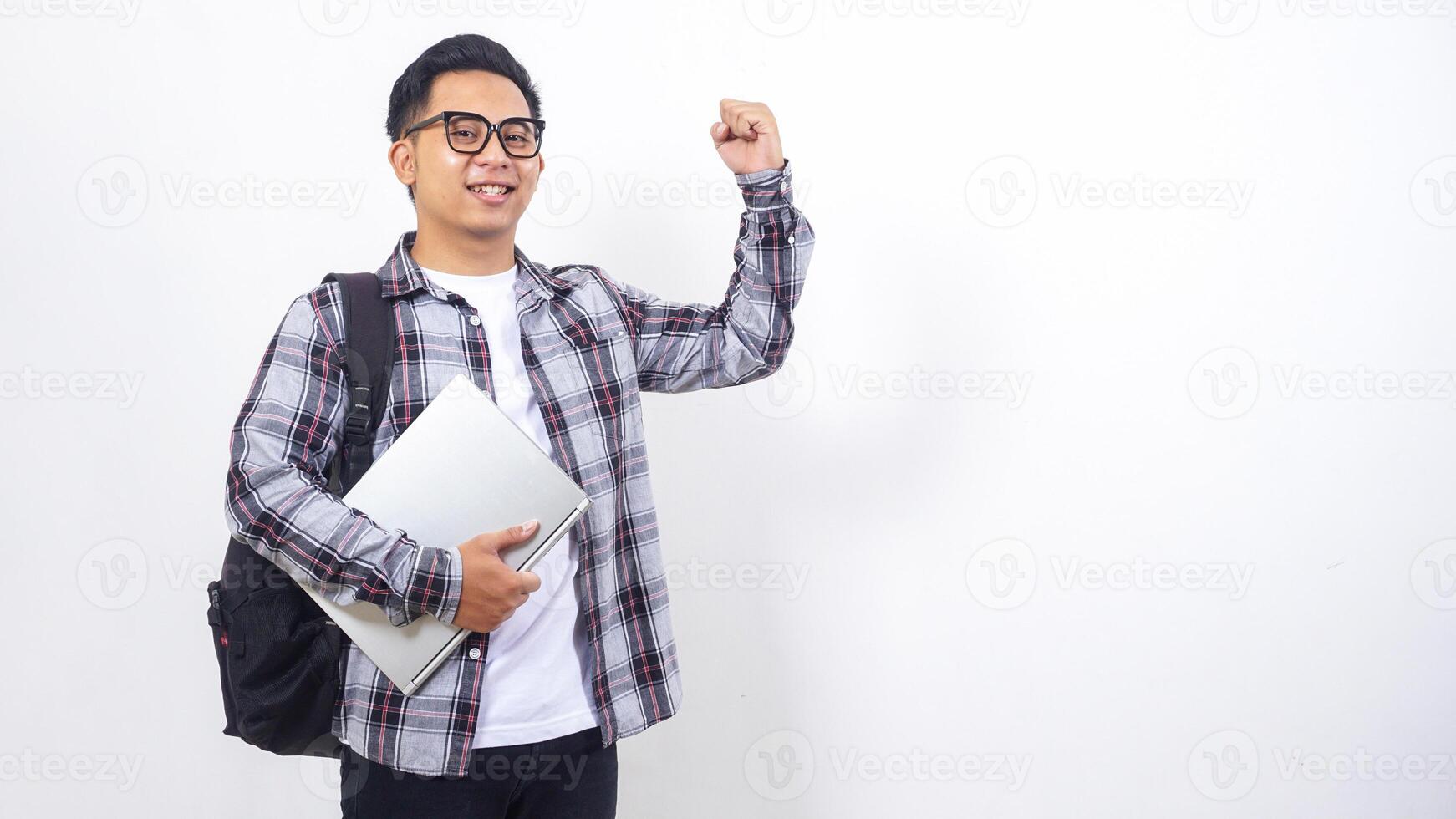 Handsome young Asian male college student with a backpack and holding laptop netbook while showing his fist isolated on white background photo