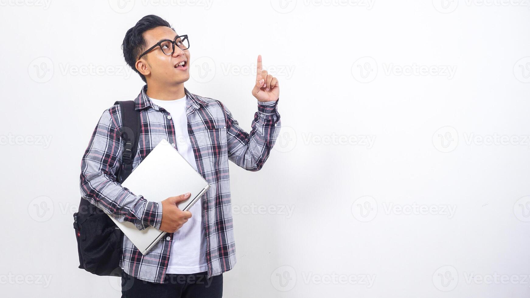 Portrait of handsome young Asian male college student with a backpack and holding laptop netbook while showing gesture of number one isolated on white background photo