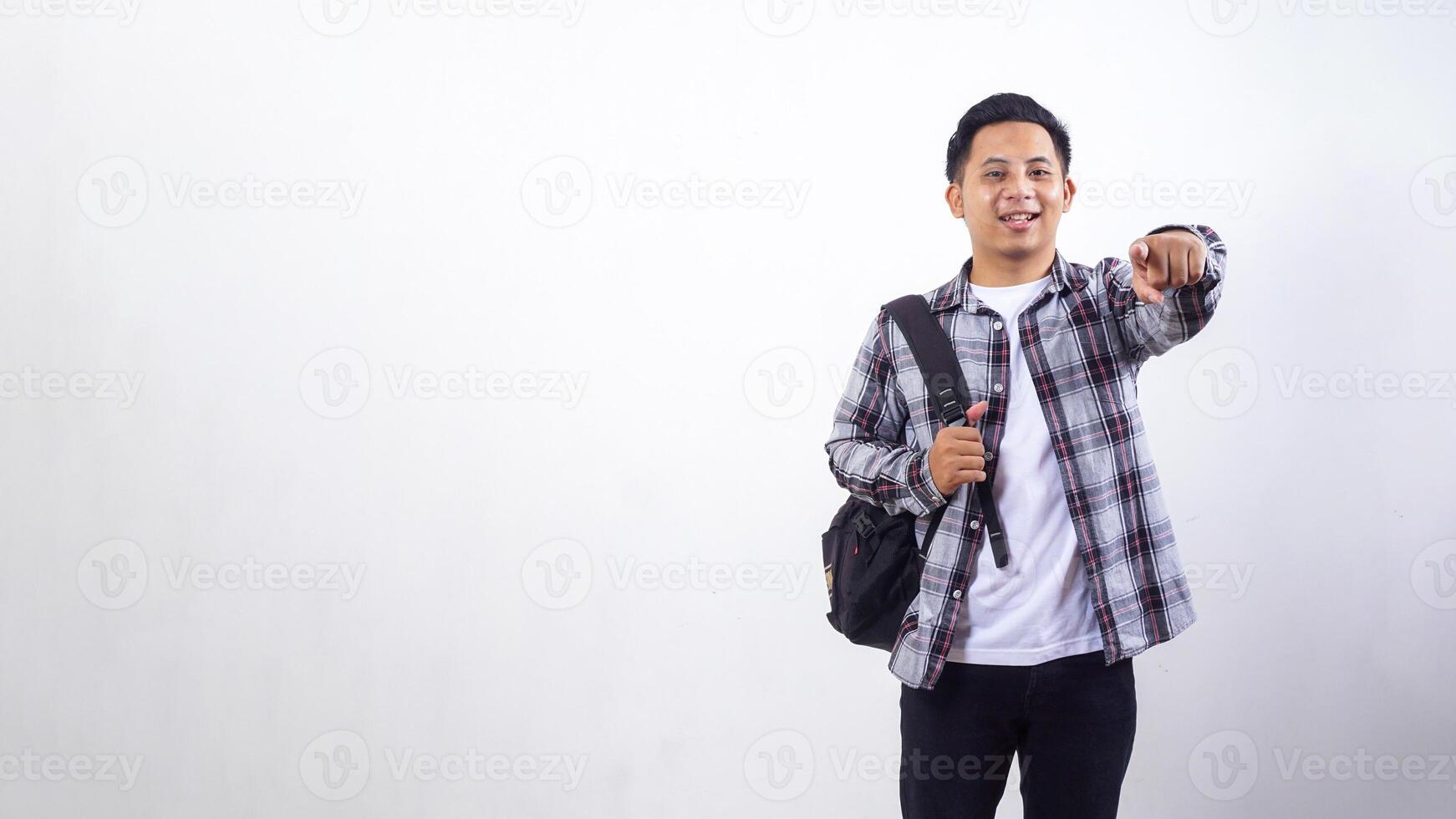 Handsome young Asian male college student with a backpack and showing his finger pointing to camera isolated on white background photo