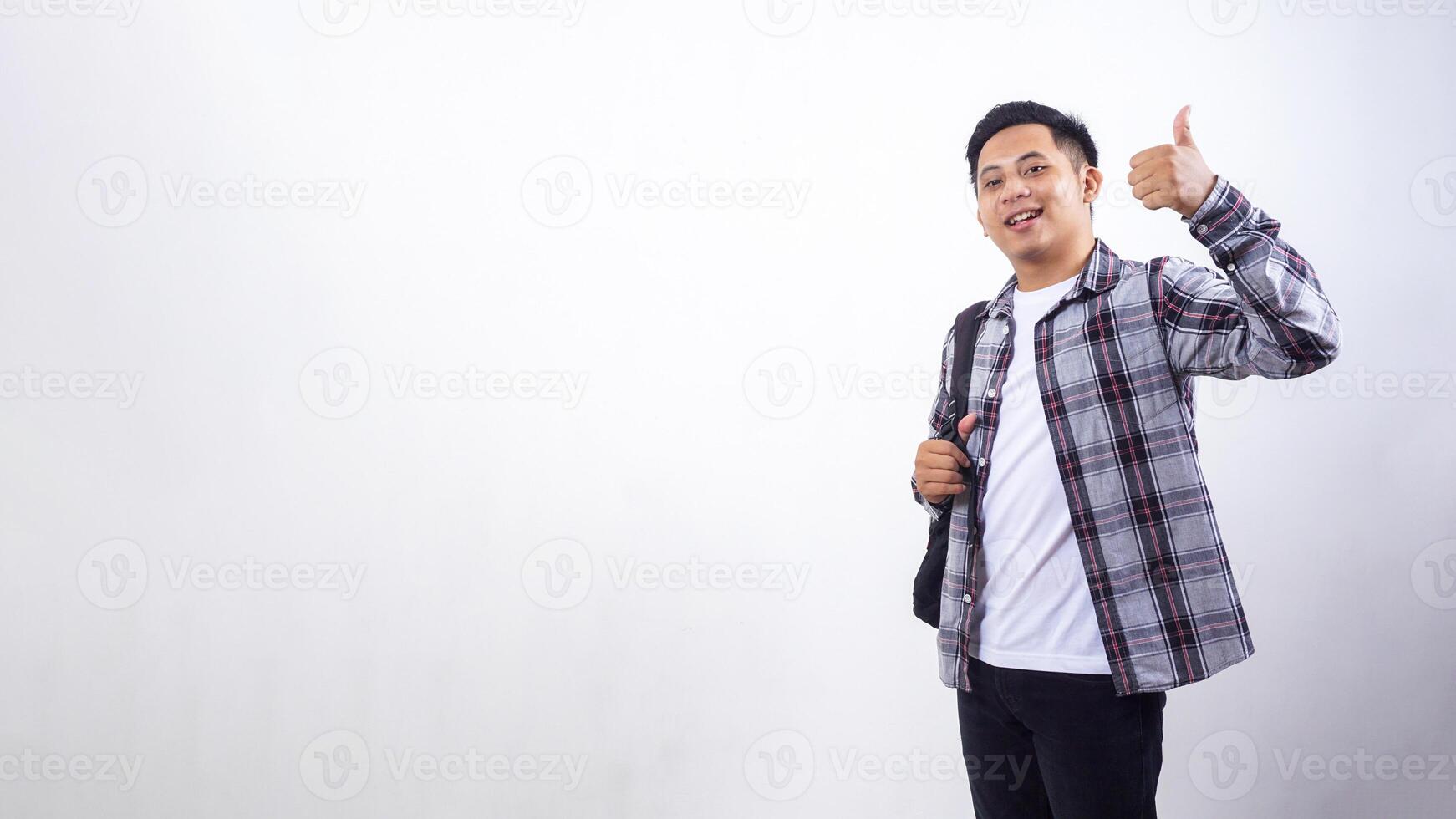 Handsome young Asian male college student with a backpack and showing his thumb up isolated on white background photo