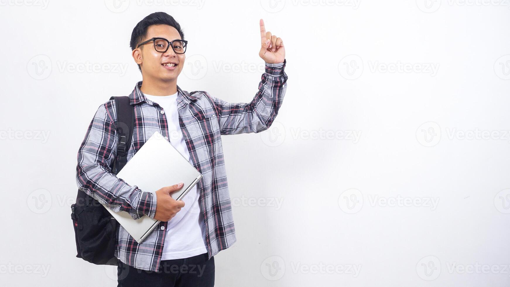 Handsome young Asian male college student with a backpack and holding laptop netbook while showing gesture of number one isolated on white background photo