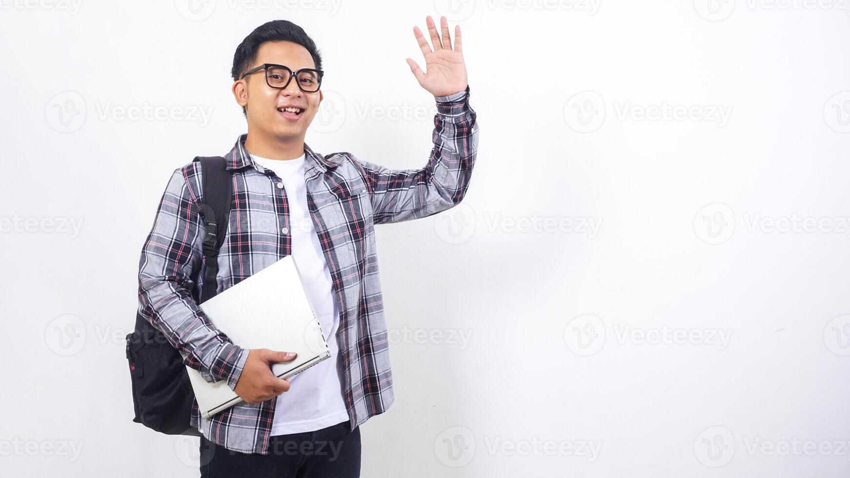 Handsome young Asian male college student with a backpack and holding laptop netbook while showing gesture of greeting isolated on white background photo