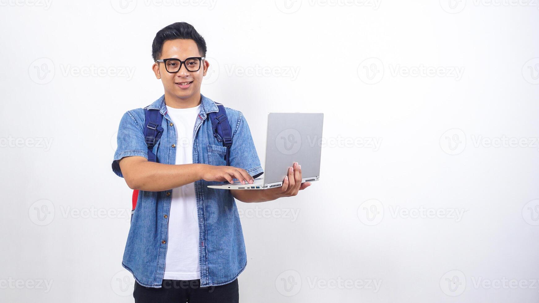 Young Asian male university student in casual outfit with backpack and open laptop isolated on white background with copy space photo