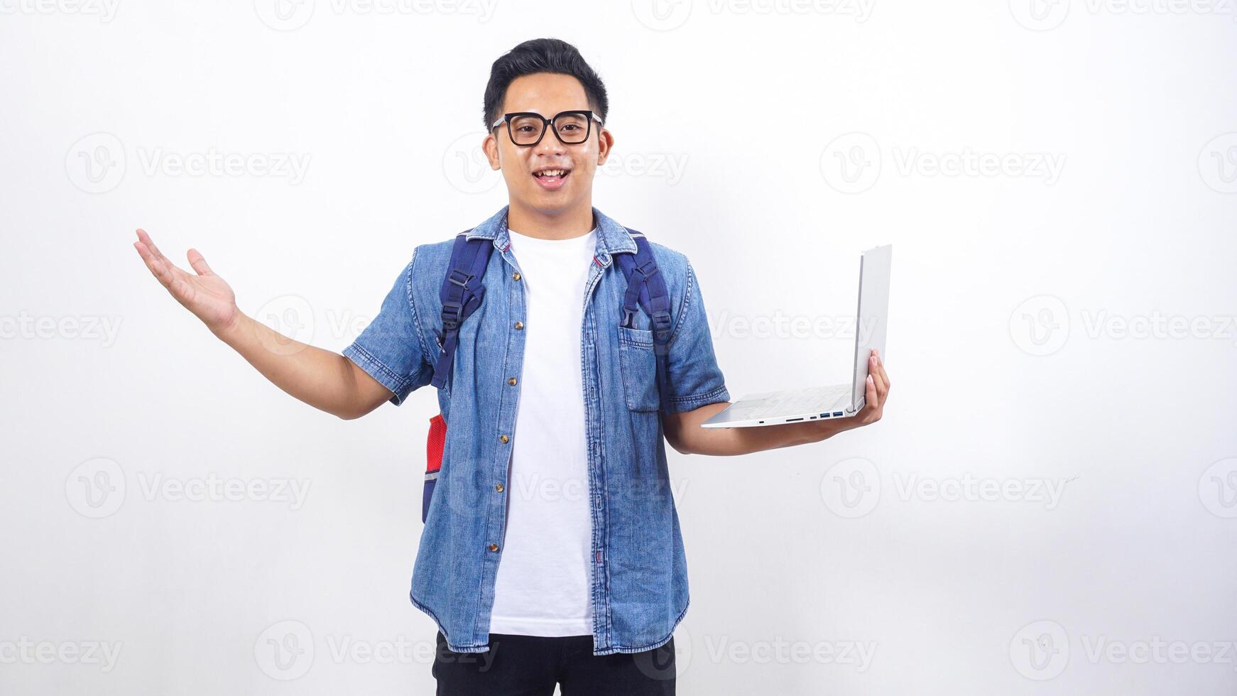 Smiling young Asian male university student in casual outfit with backpack and holding open laptop isolated on white background with copy space photo