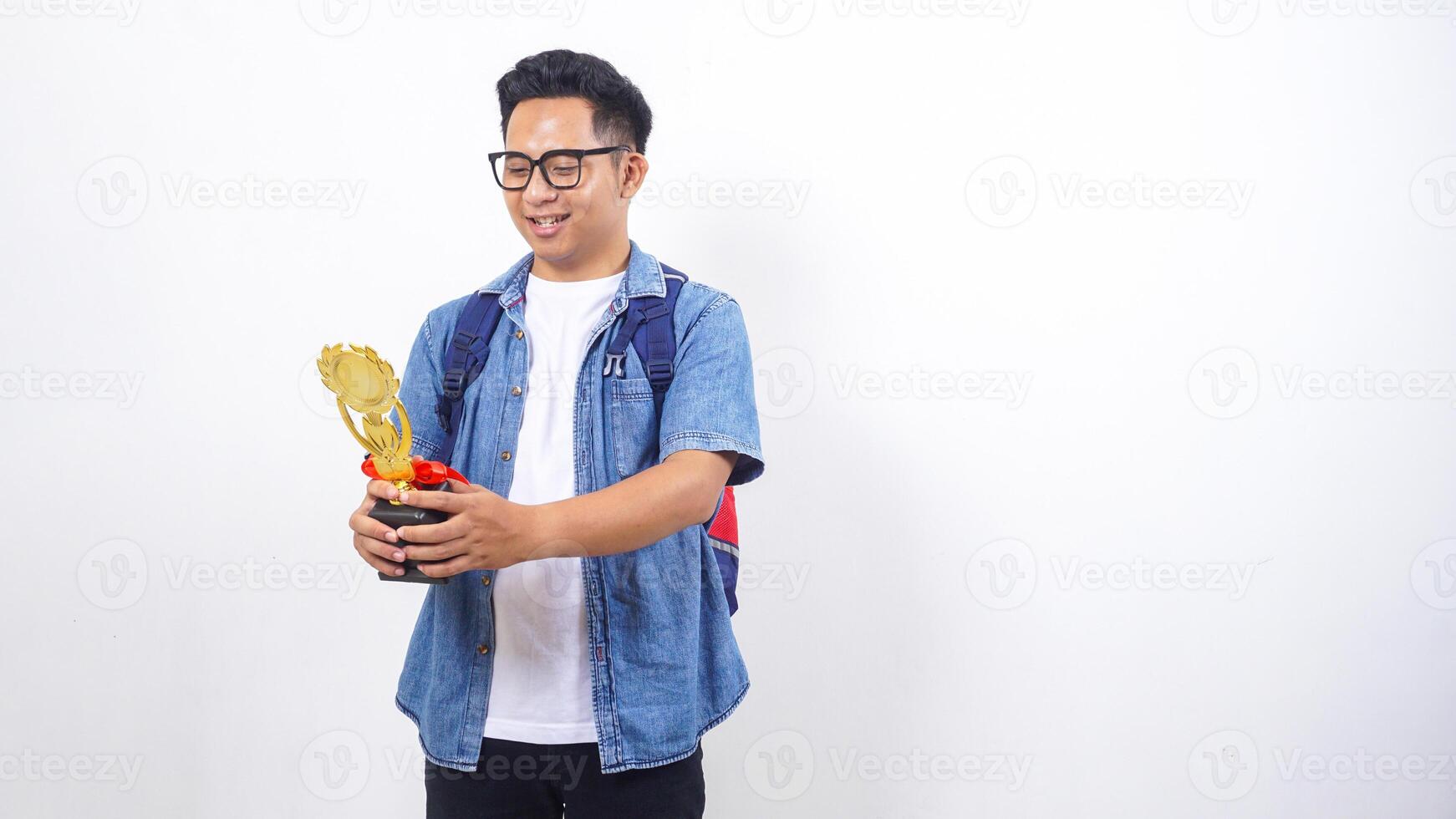 Portrait of young Asian male university student in casual outfit with backpack is holding trophy isolated on white background photo