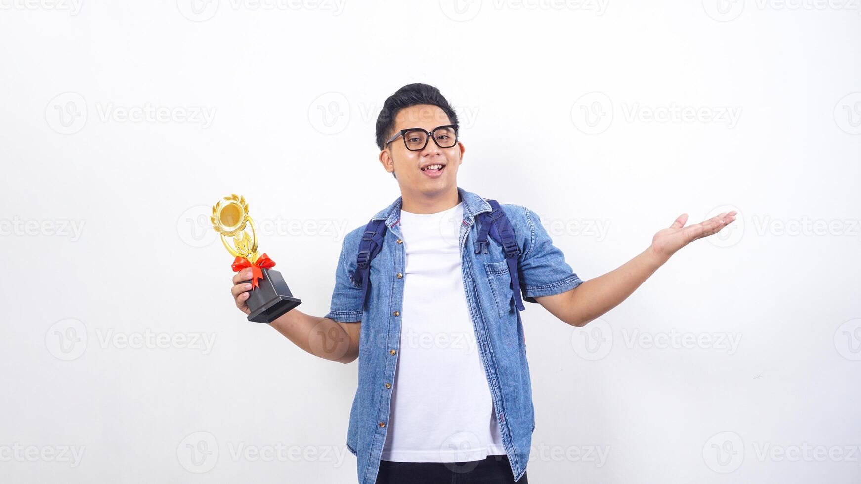 Portrait of smiling young Asian male university student in casual outfit with backpack is holding trophy isolated on white background photo