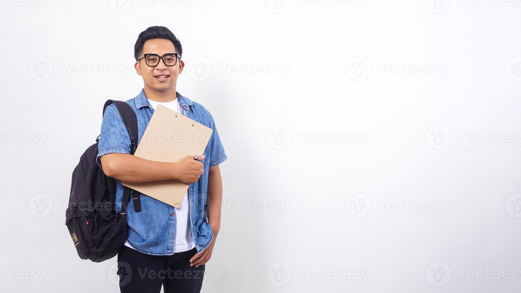 Portrait of young Asian male university student in casual outfit with backpack and clipboard isolated on white background photo