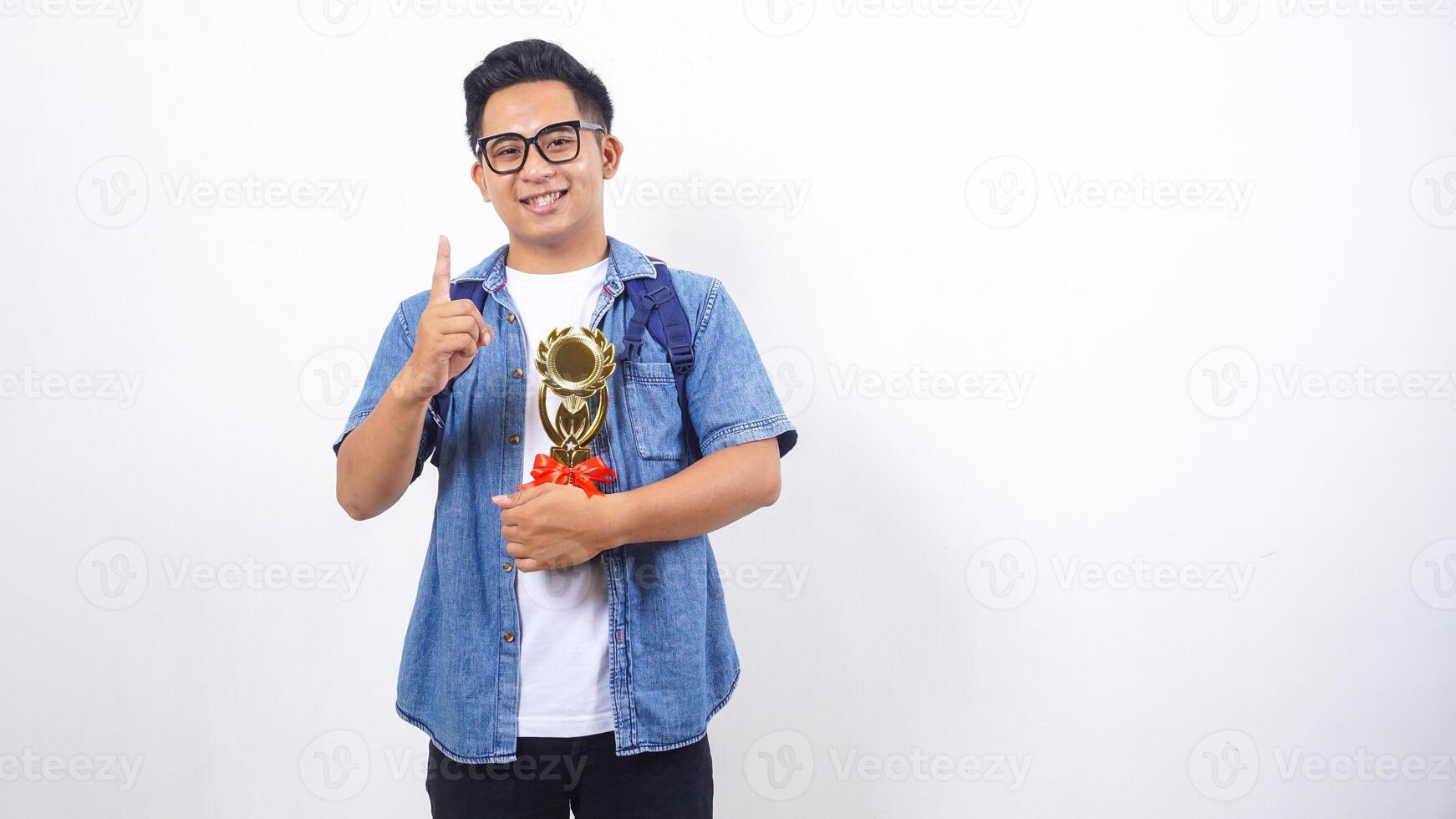 Handsome young Asian male university student in casual outfit with backpack is holding trophy isolated on white background with copy space photo