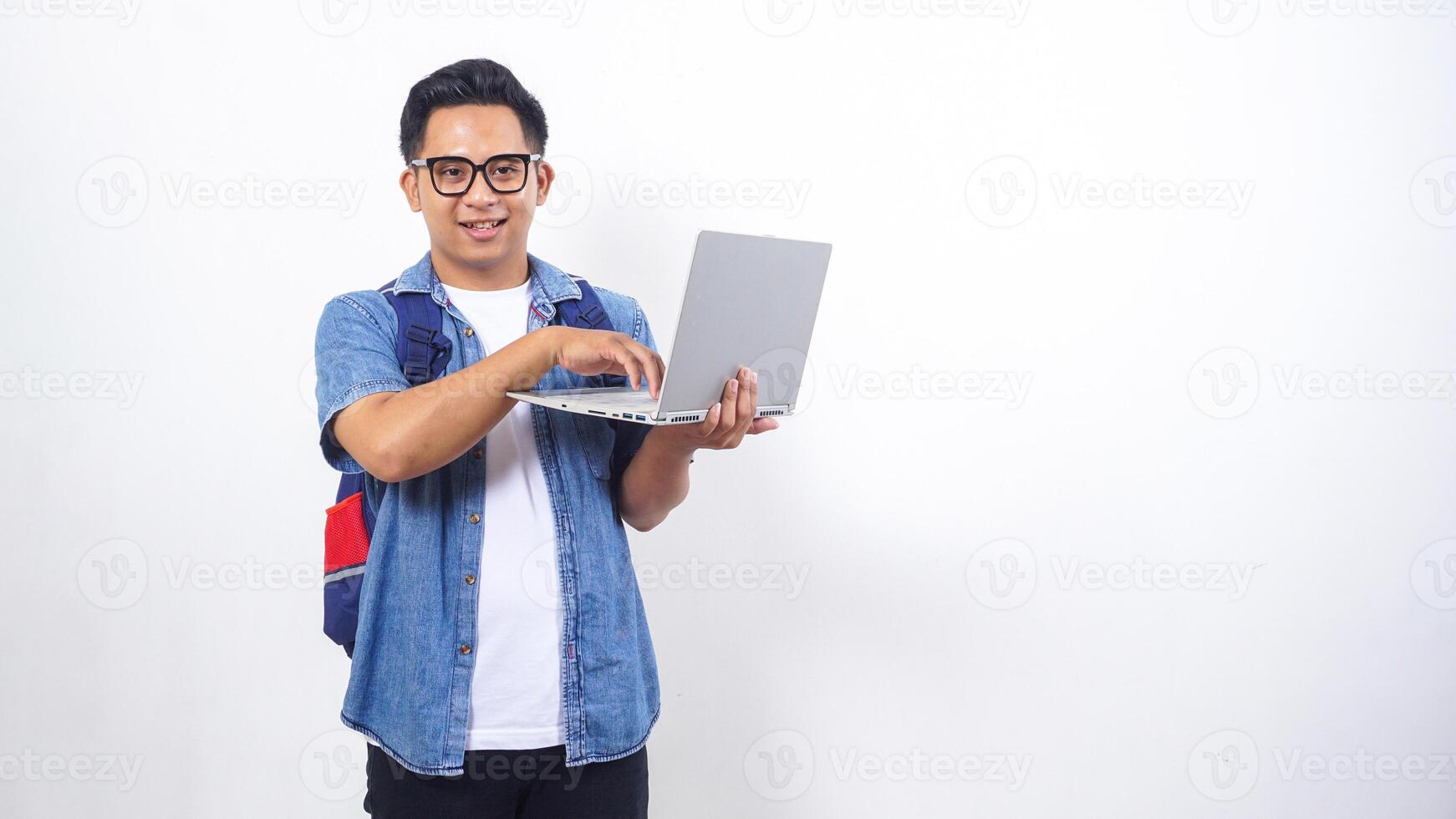 Portrait of smiling young Asian male university student in casual outfit with backpack and open laptop isolated on white background photo