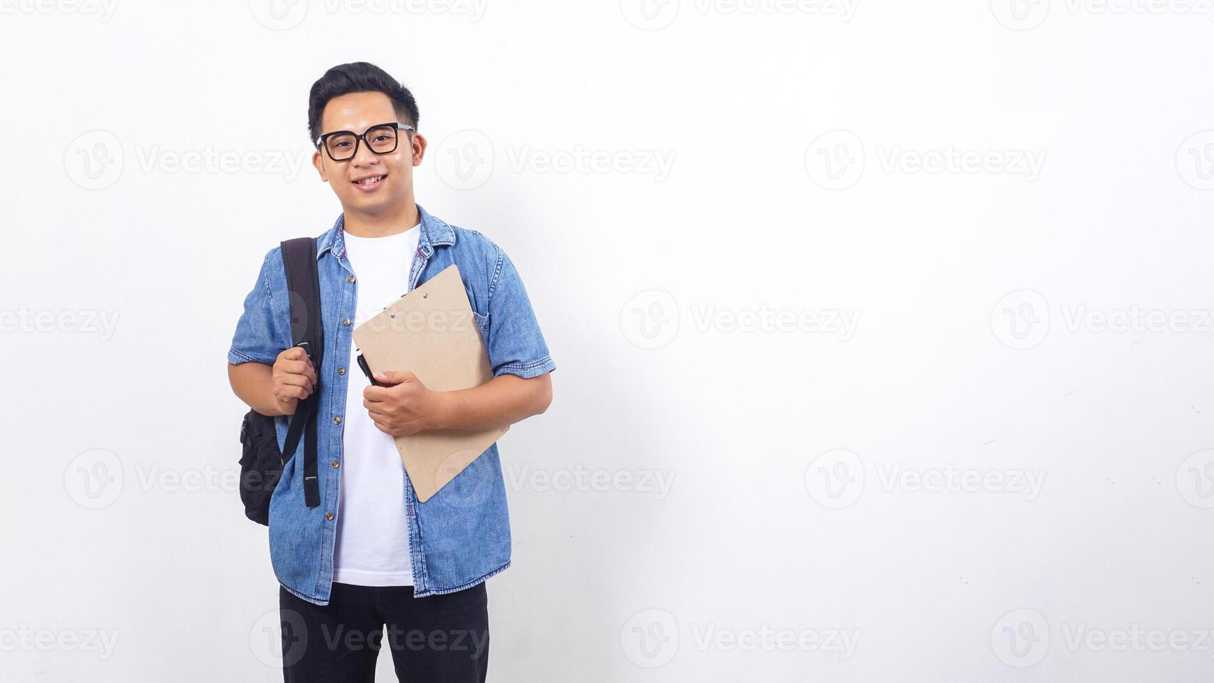 Portrait of smiling young Asian male university student in casual outfit with backpack and clipboard isolated on white background photo