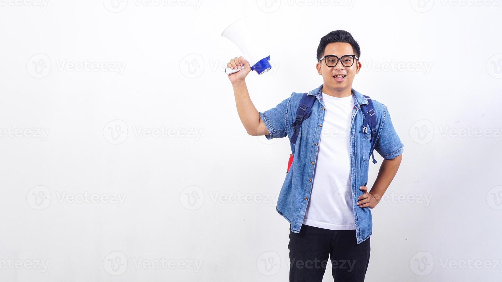 Portrait of smiling young Asian male university student in casual outfit with backpack is holding megaphone isolated on white background photo