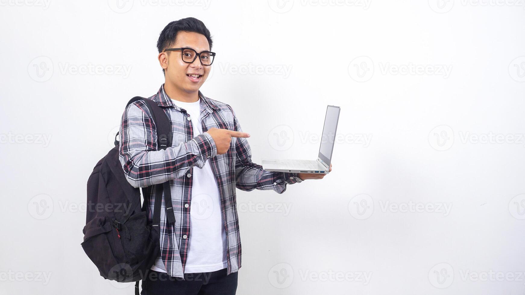 Happy young Asian male college student with a backpack and pointing his finger to open laptop notebook isolated on white background photo