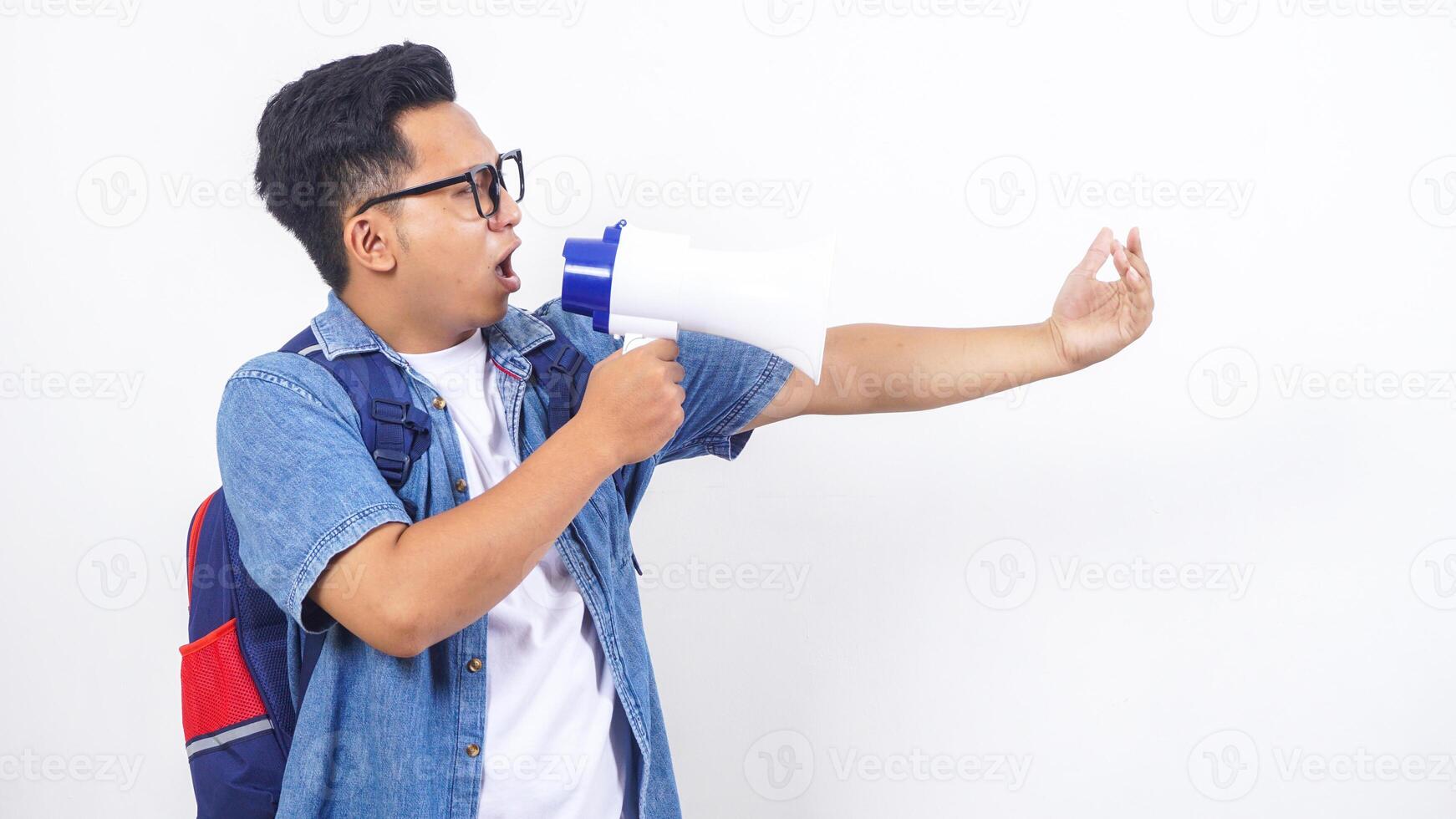Portrait of young Asian male university student in casual outfit with backpack is shouting on megaphone isolated on white background photo