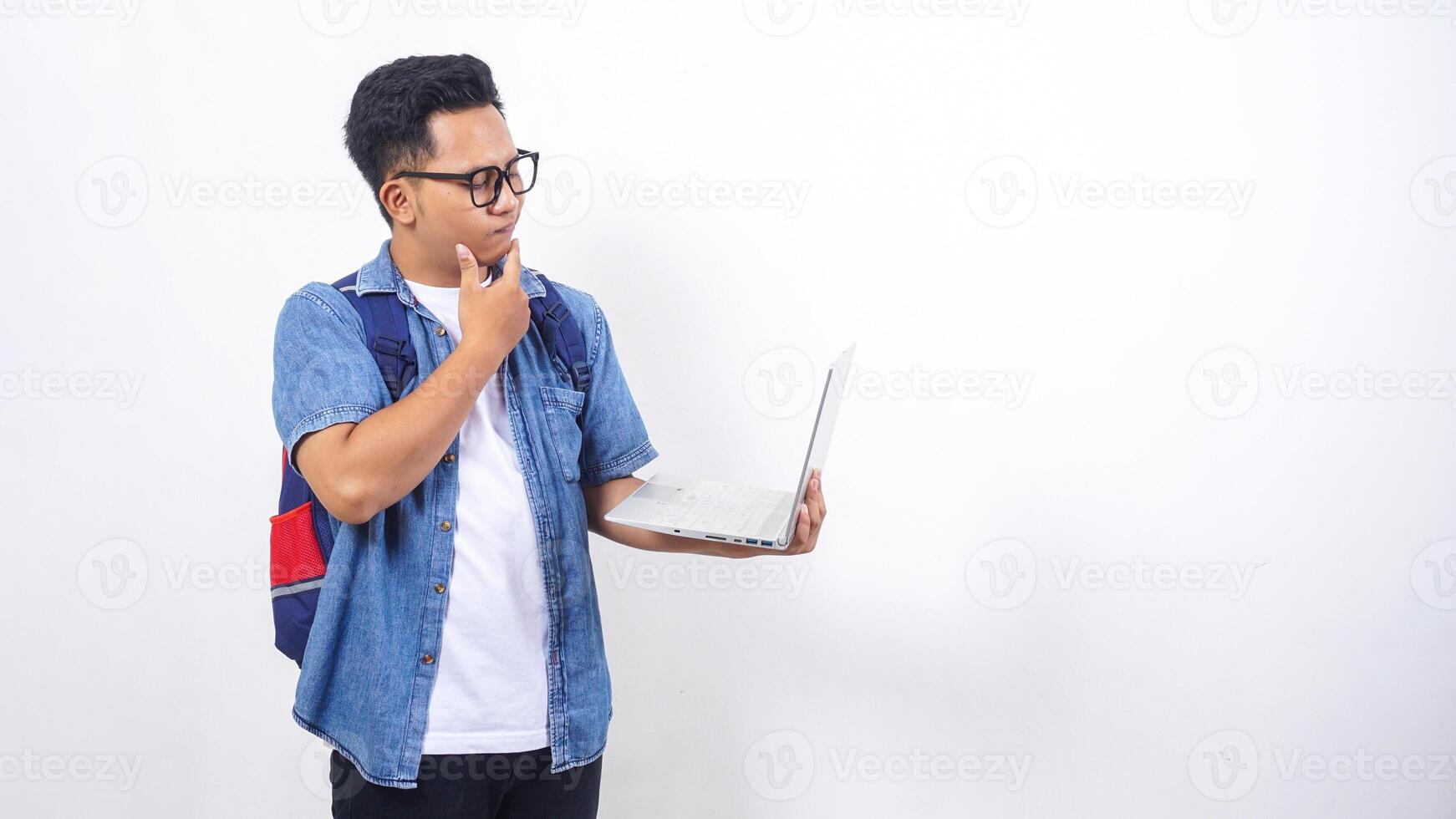 Young Asian male university student in casual outfit with backpack and holding open laptop isolated on white background with copy space photo