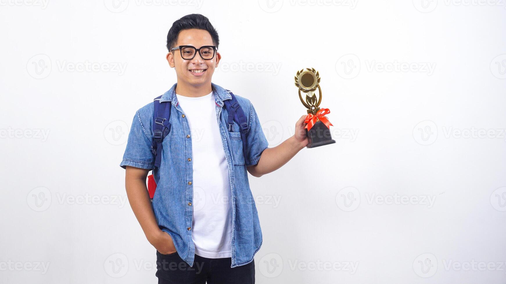 Young Asian male university student in casual outfit with backpack is holding trophy isolated on white background photo