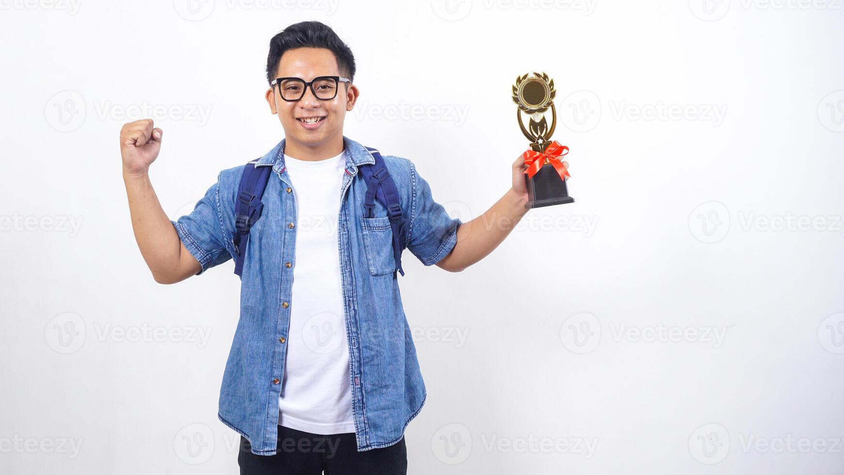 Handsome young Asian male university student in casual outfit with backpack is holding trophy isolated on white background photo