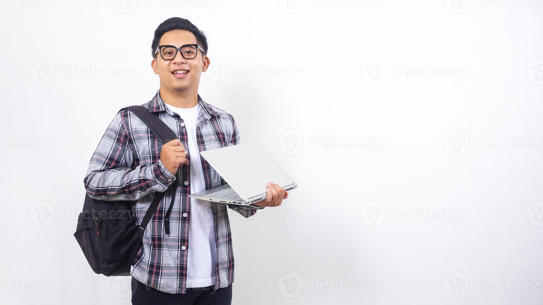 Portrait of happy young Asian male college student with a backpack and holding open laptop with casual pose isolated on white background photo