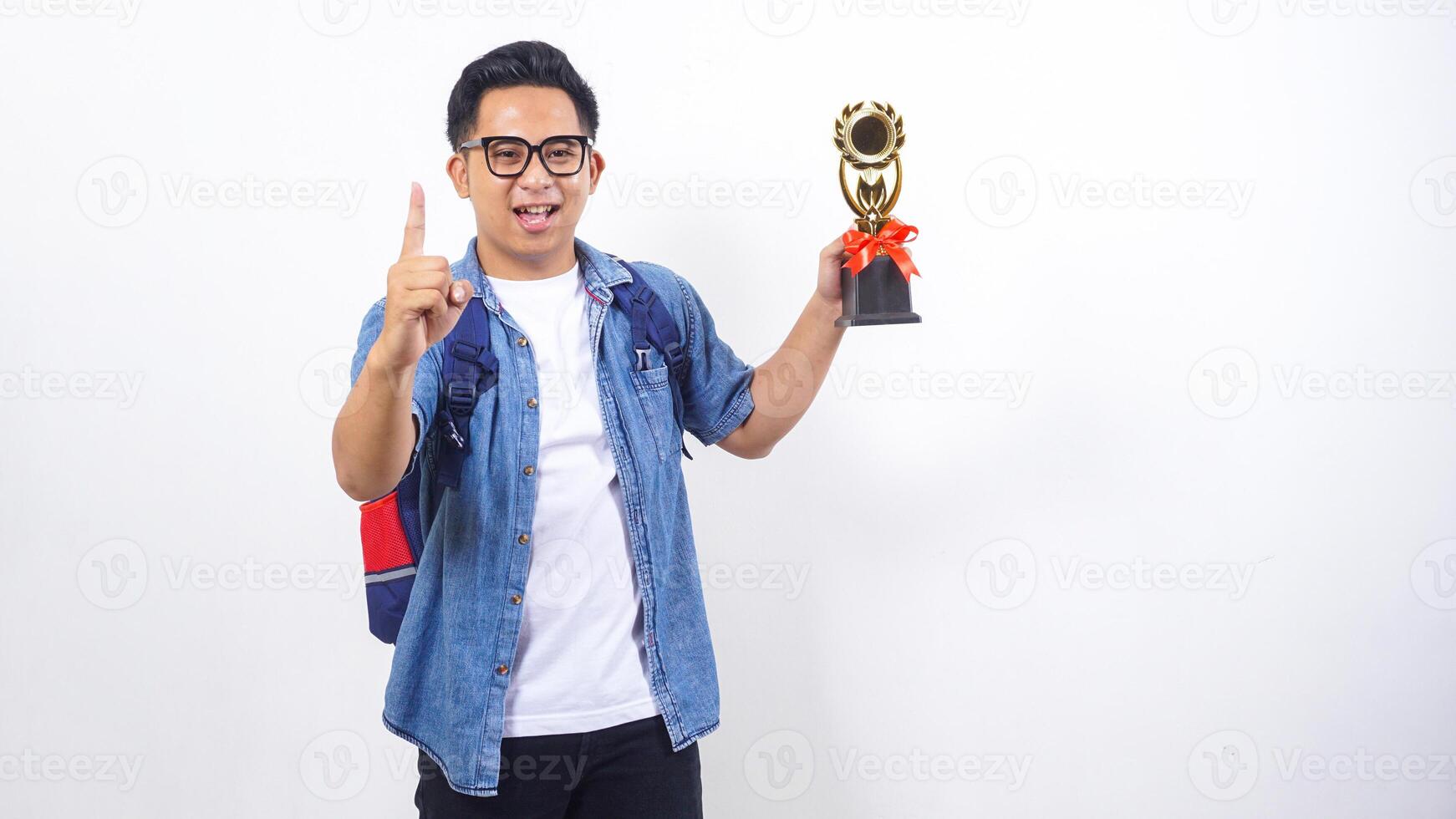 Portrait of excited young Asian male university student in casual outfit with backpack is holding trophy isolated on white background photo