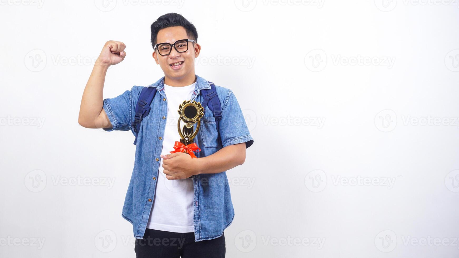 Happy young Asian male university student in casual outfit with backpack is holding trophy isolated on white background with copy space photo