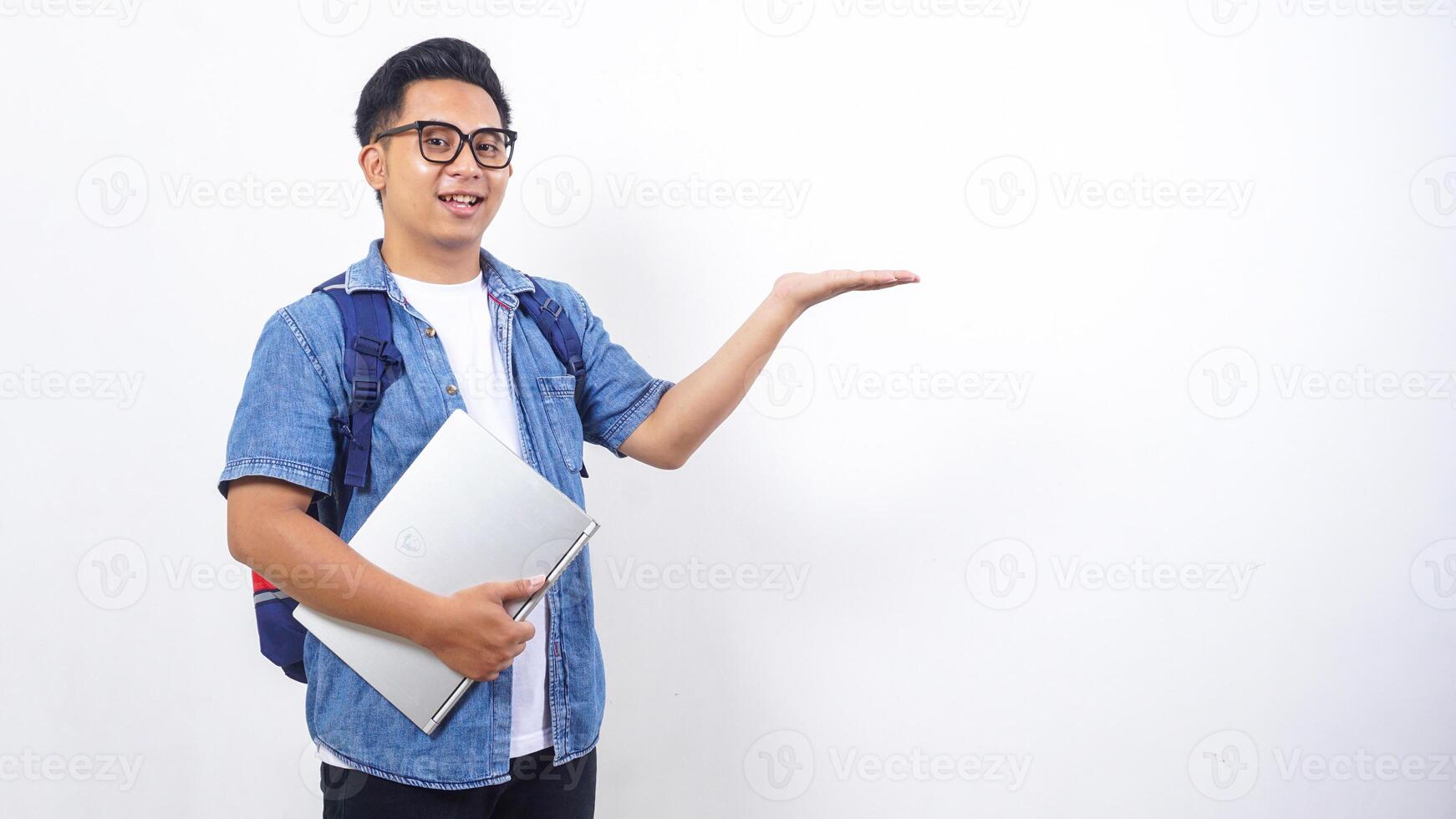 Portrait of smiling young Asian male university student in casual outfit with backpack and laptop isolated on white background with copy space photo