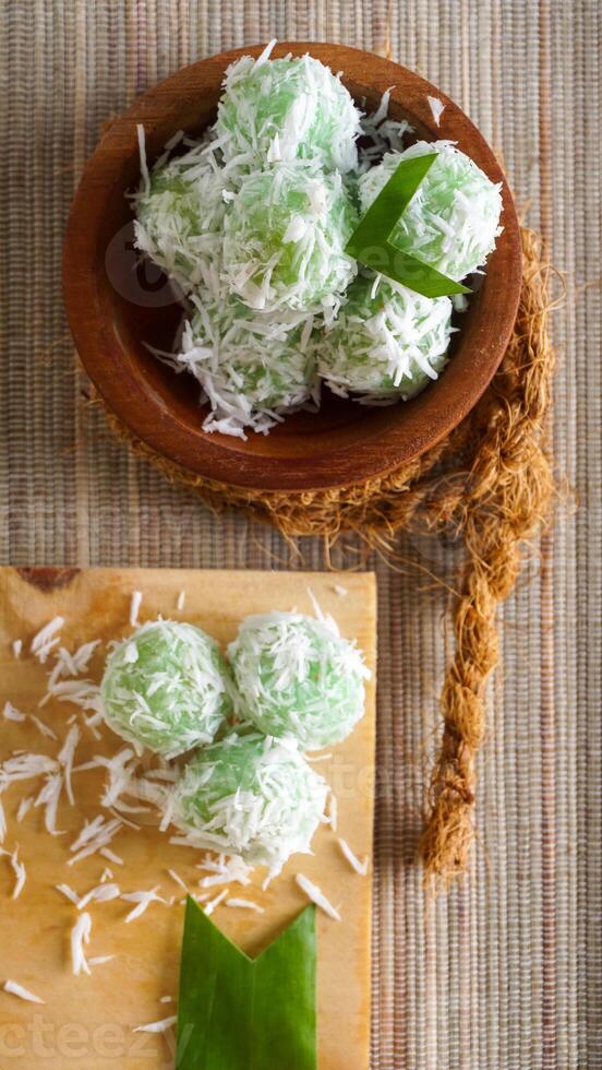 A traditional Indonesian snack made from green sticky rice balls and rolled in grated coconut called Klepon on wooden platter isolated on white background photo