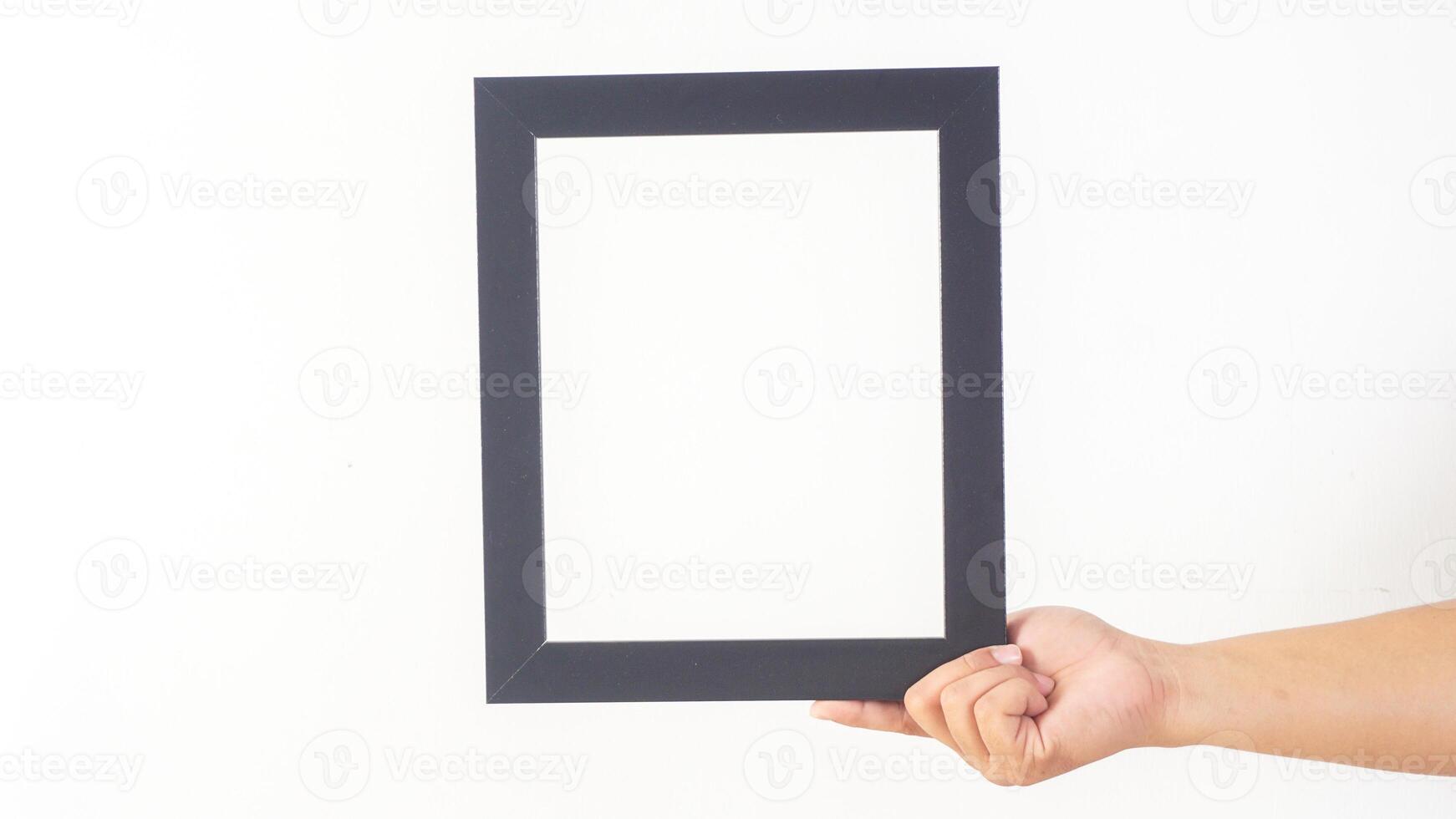 Hand holding simple black colored wooden picture frame isolated on white background photo