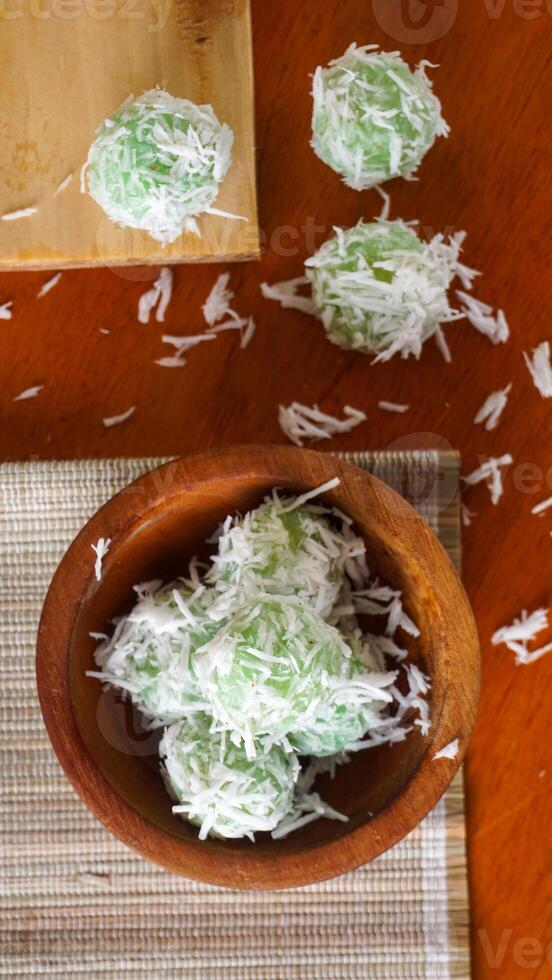 Klepon is a traditional Indonesian snack made from green sticky rice balls and rolled in grated coconut on wooden bowl isolated on white background photo