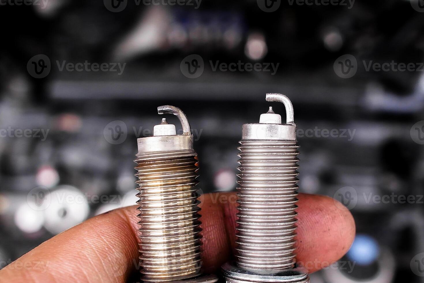 Comparison of used and new spark plugs, A hand holds old and new spark plugs in front of a blurred car engine. Automotive maintenance and ignition parts. photo