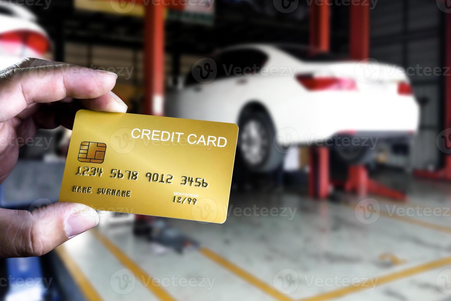 Paying for Car Repair , A hand holds a gold credit card in a car repair shop with a vehicle lifted on a hydraulic lift. Paying for service. photo