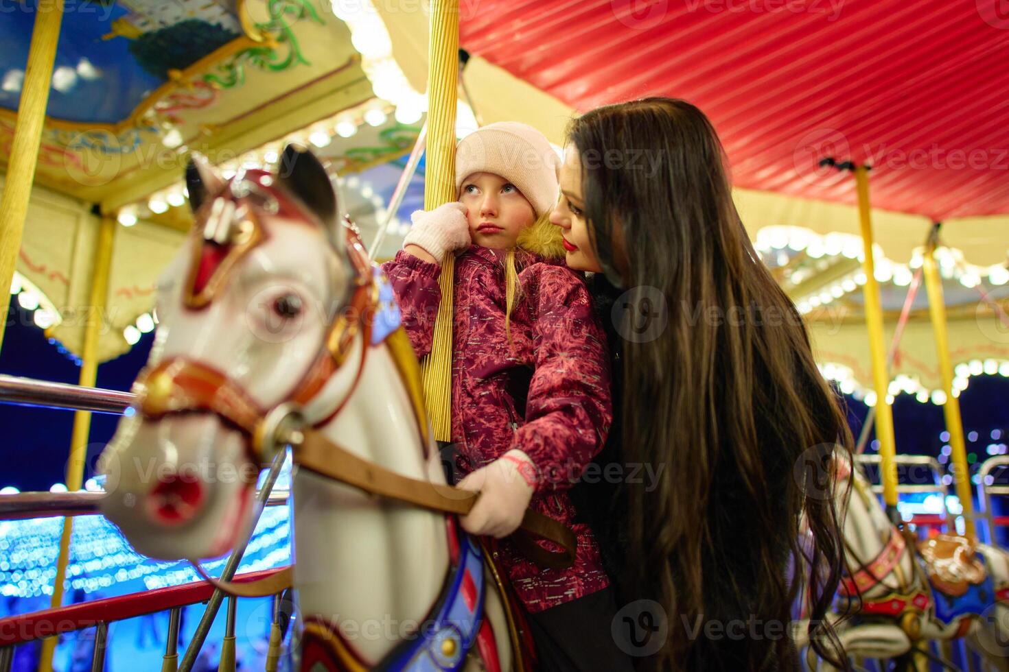 Joyful mother and daughter share a moment on a carousel at night photo