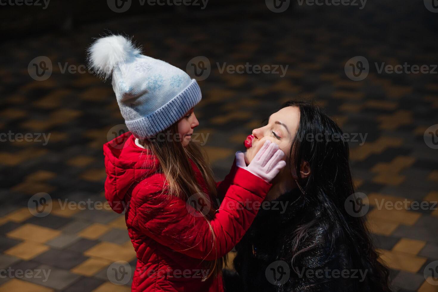 Mother and daughter share a playful moment outdoors at night during winter, capturing joy and warmth photo