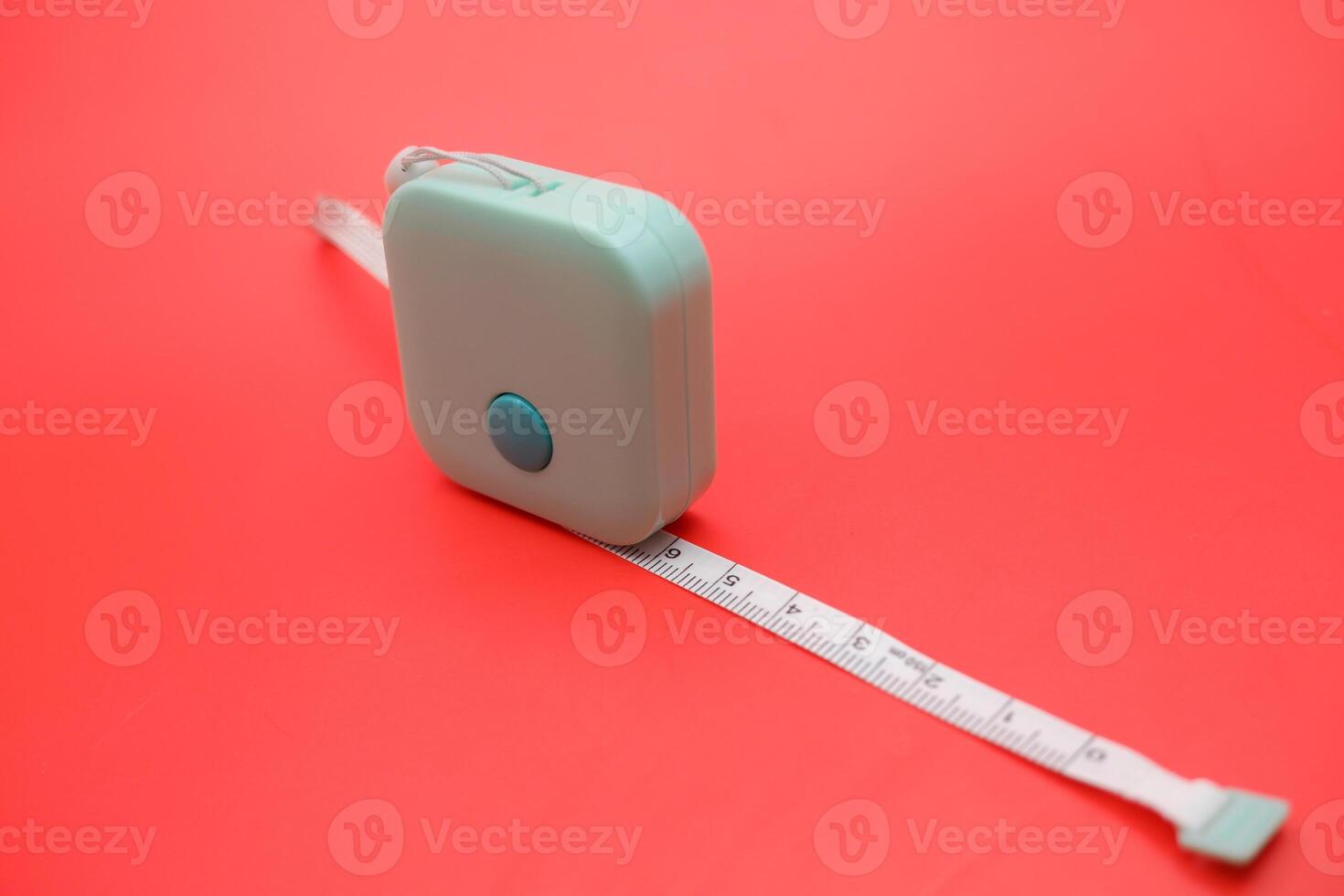 Flexible green measuring tape rolled neatly against a red background. Clean studio shot with strong contrasting colors. photo