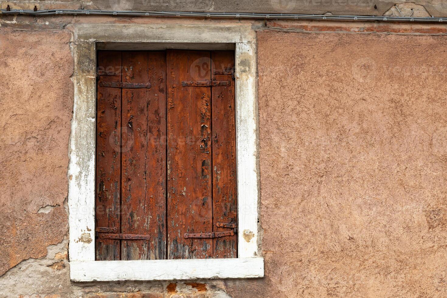 Old rustic window with weathered wooden shutters on textured wall photo