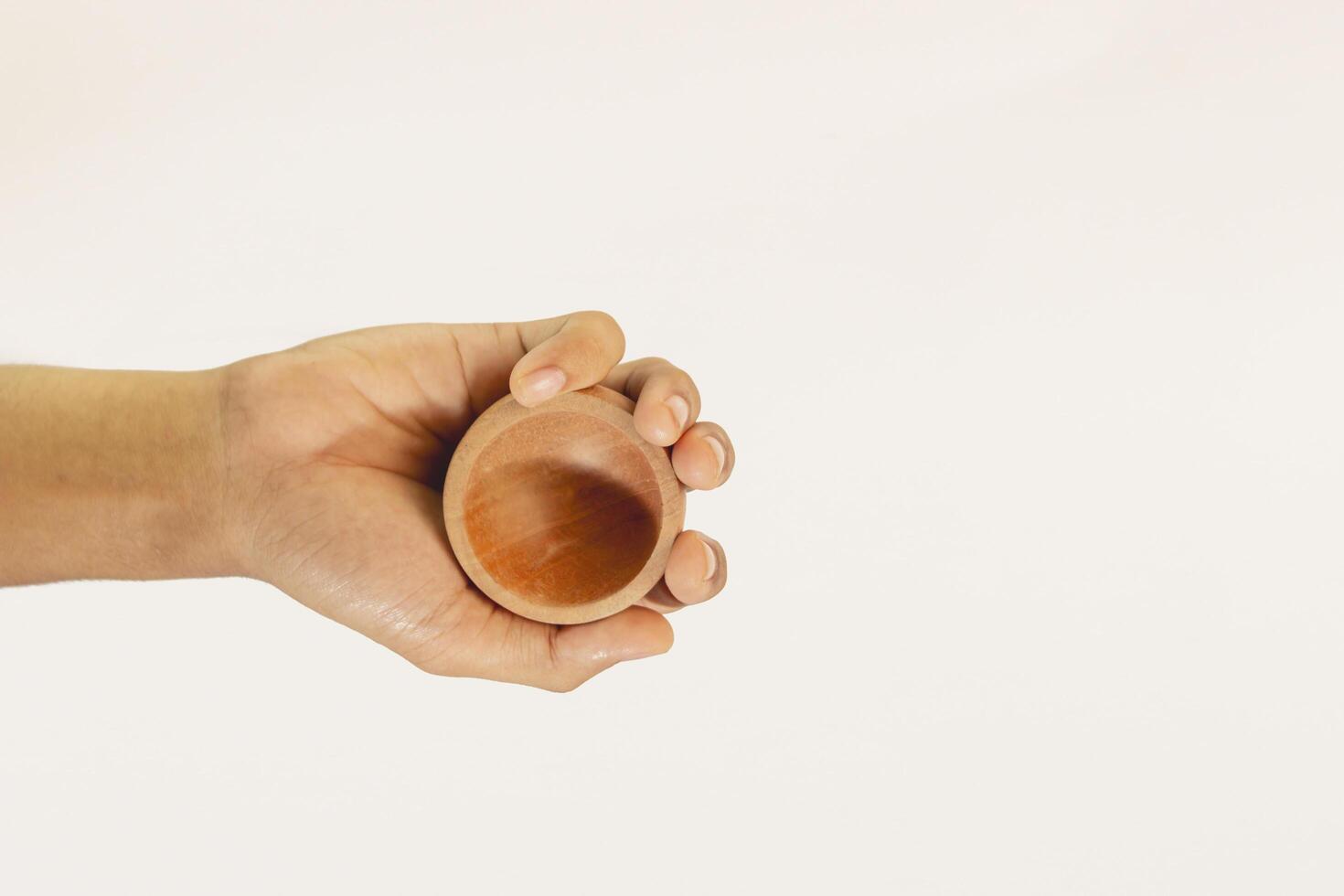 hand holding small wooden bowl. small bowl made of light brown wood looks simple isolated on white background. photo