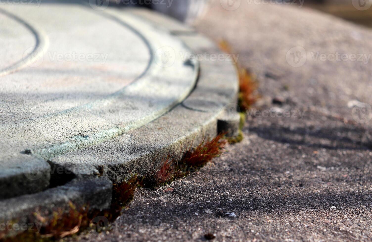 Fragment of stone well cover, grainy texture of stone, concrete with red moss on surface in sunlight photo
