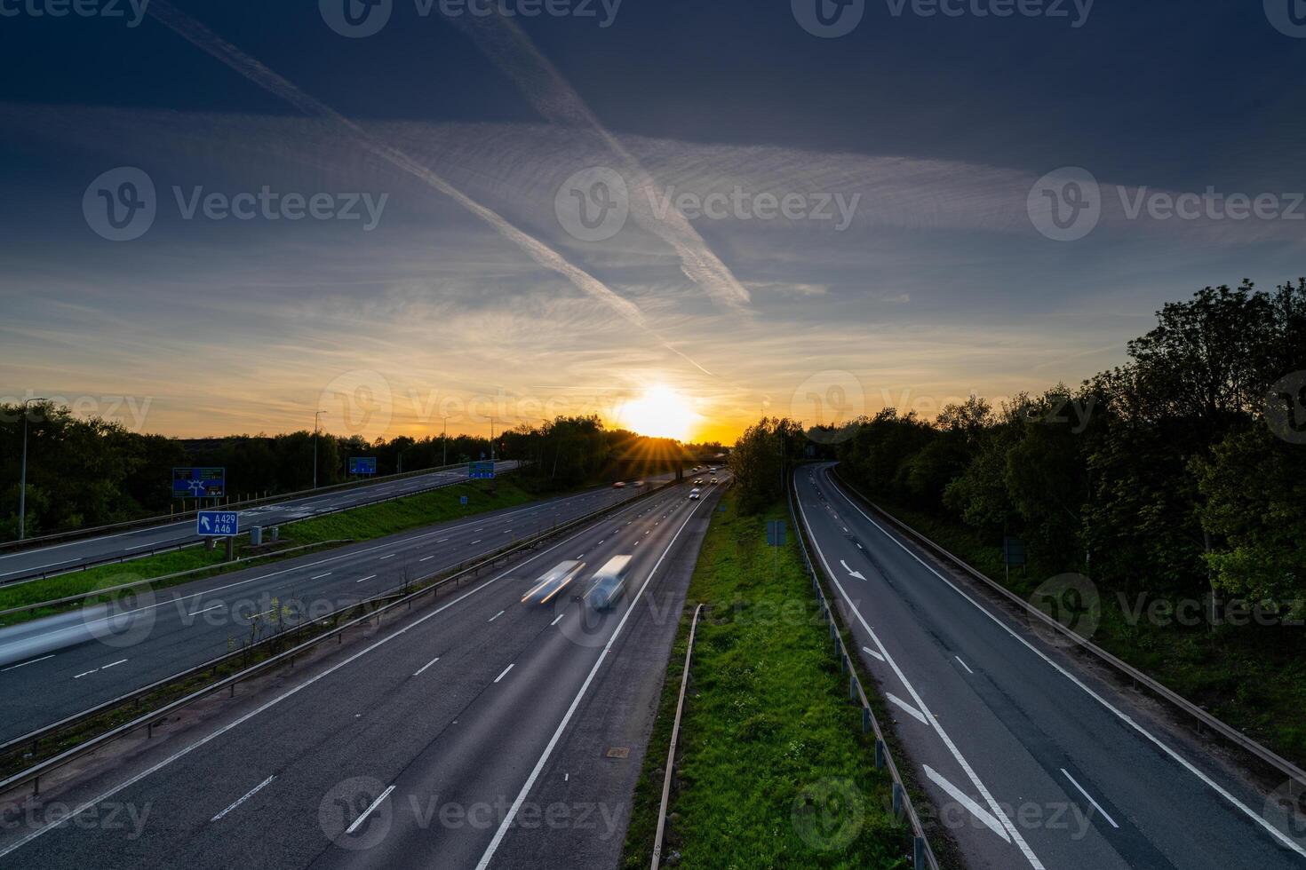 Cars driving fast on highway at sunset with contrails in the sky photo