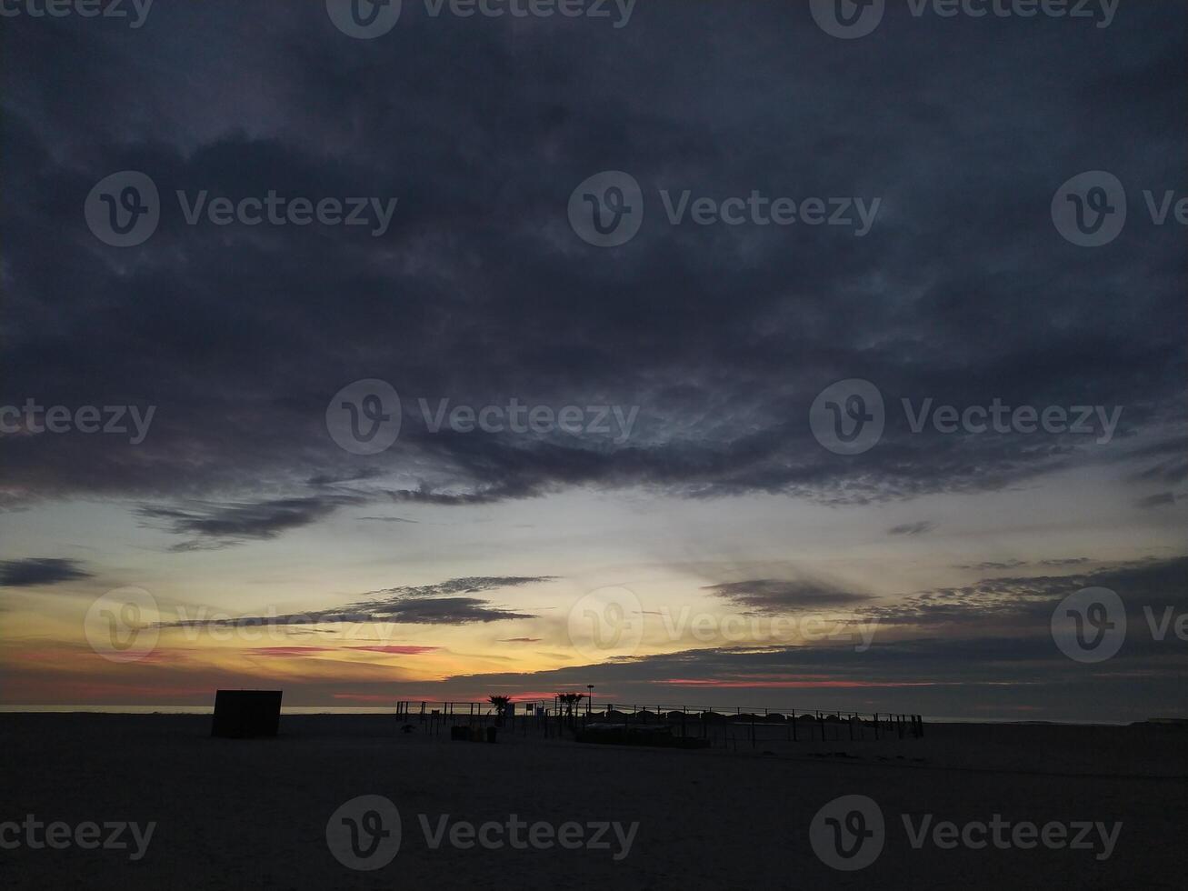 Serene beach sunset. Dark silhouettes against a vibrant, colorful sky. Perfect for travel, nature, or tranquility themes. Evokes peace and the end of day. photo