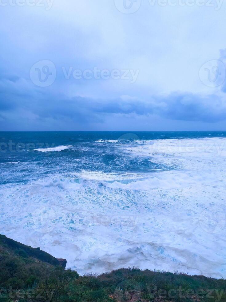 Dramatic seascape featuring turbulent waves crashing against a rugged coastline under an overcast sky. Powerful natural scenery. Ideal for themes of resilience or raw beauty. photo